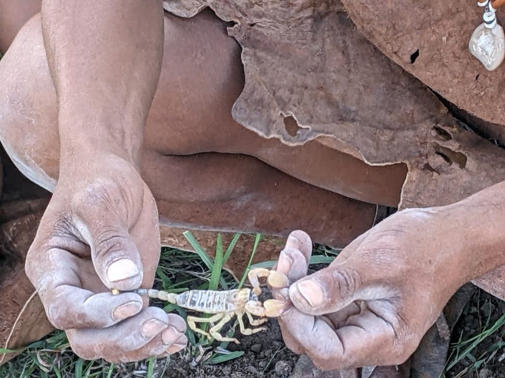 One of the men holding a scorpion by its tail and claws.