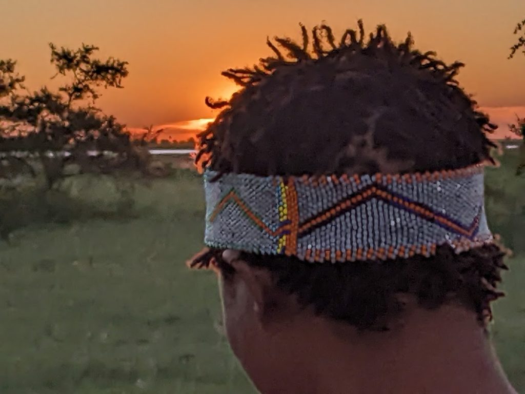 Man wearing a beaded headband, mostly blue with orange around the edges, and an orange zig-zag bordered in black.