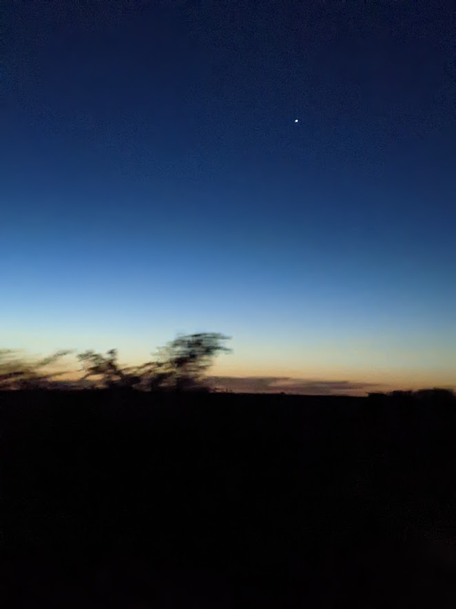 The planet Venus in its role as the Evening Star, in a deep-blue sky that gradually lightens toward the remains of a sunset on the horizon.