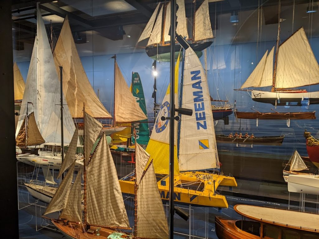 A profusion of boats. The closest is a gaff-rigged ketch; behind it are a modern-looking sloop and a yellow catamaran with "Zeeman" written on its mainsail.