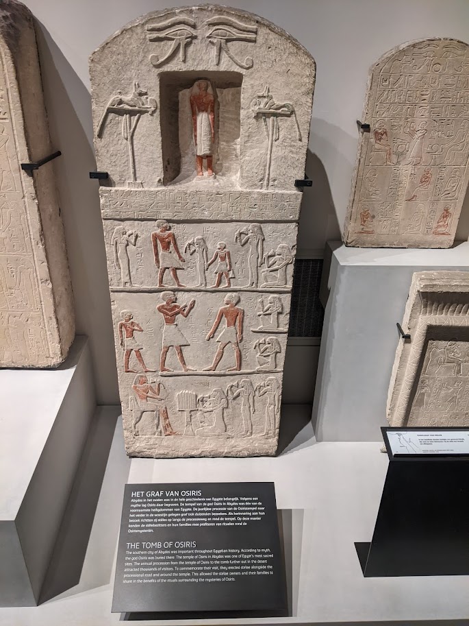 A rectangular slab of stone with a rounded top  Two eyes of Horus are above a deep niche containing a human figure, with a jackal on either side. Below these are a row of carved heiroglyphics and three rows of humanfigures.