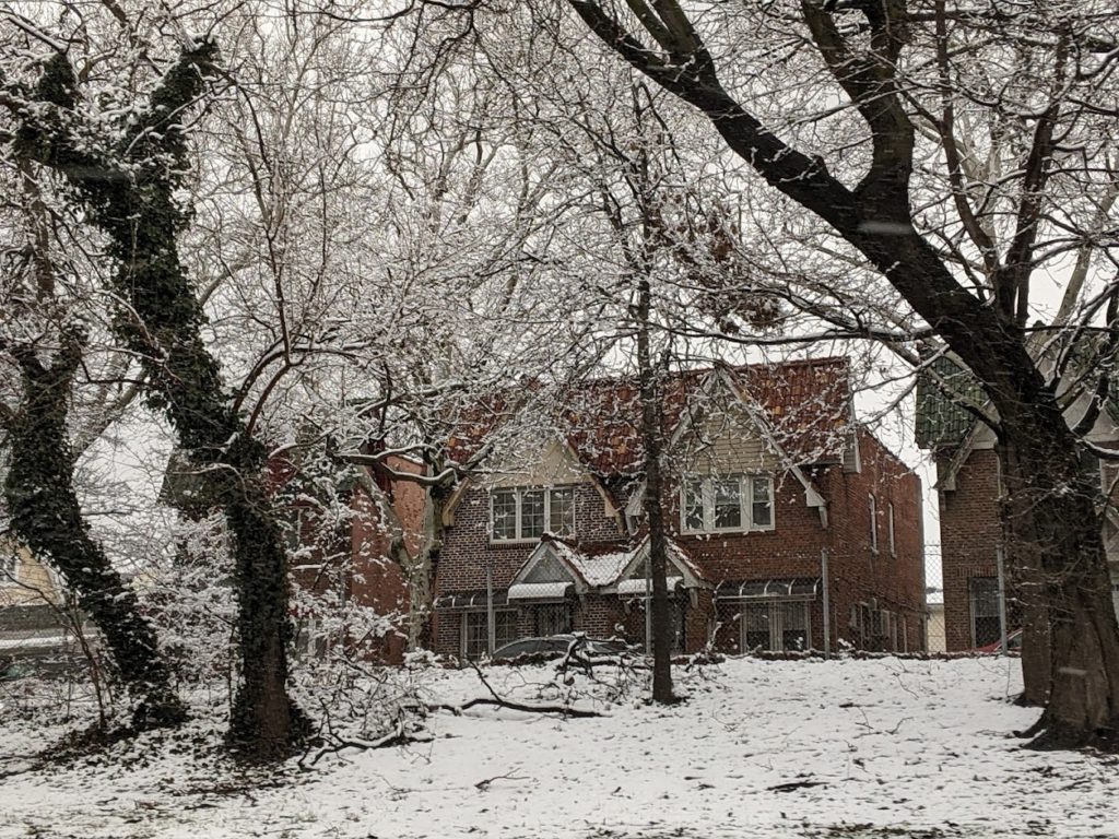 A large brick building behind three large trees and a snow-covered lawn.