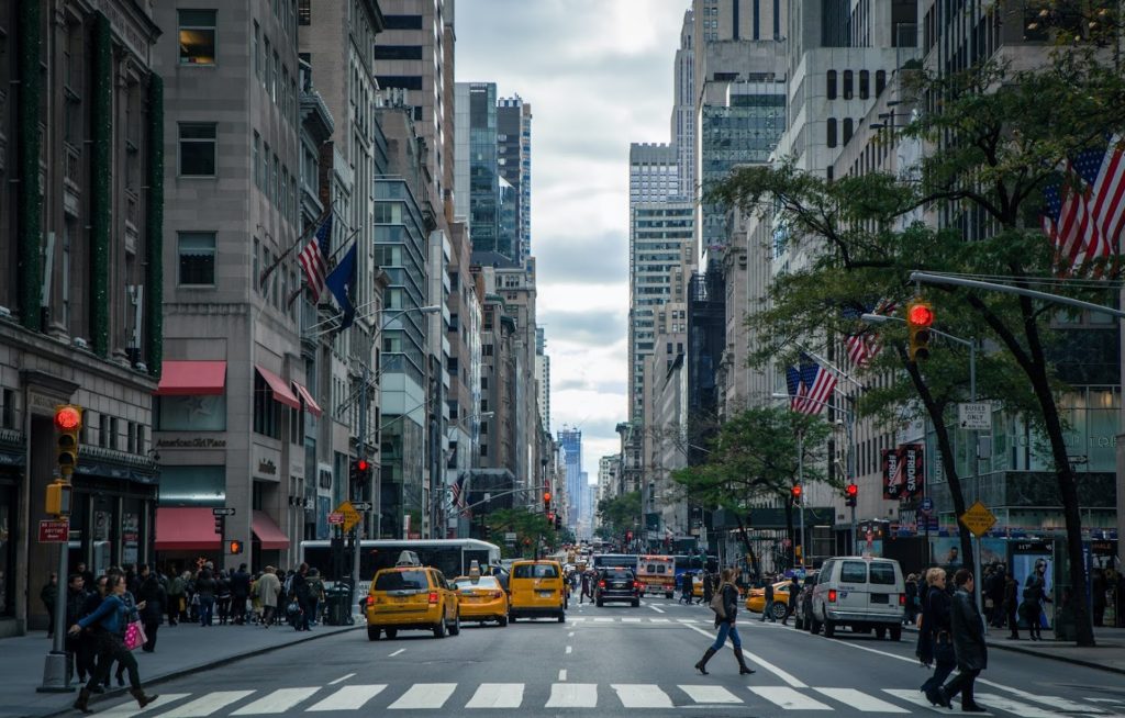 Stock photo of a Manhattan street. There is a crosswalk in the foreground, there are three yellow cabs and a few cars stopped at the other end of the block.