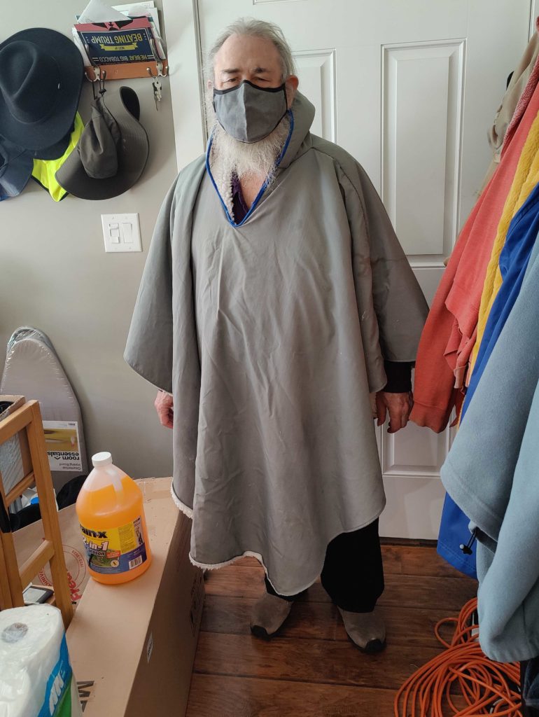 Steve standing by the door wearing a grey cape.  Some of the white lining is visible around the bottom edge, and there is blue trim around the hood.