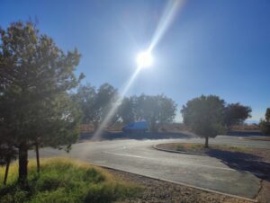 The sun glares over a rest stop parking lot. A few trees provide inadequate shade.